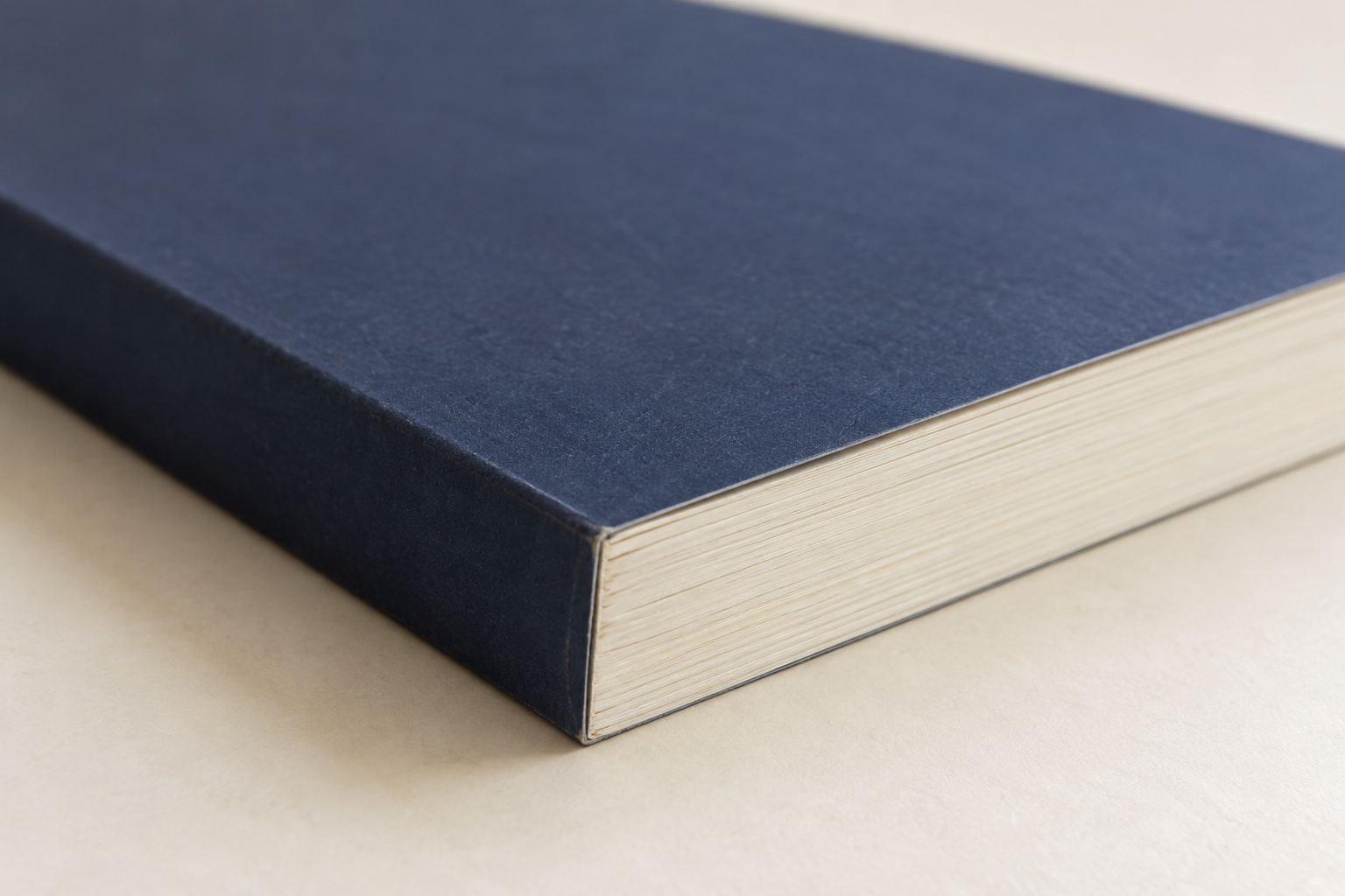 Close-up van een gesloten softcoverboek met donkerblauwe omslag, boekrug en crèmekleurige paginasneden.